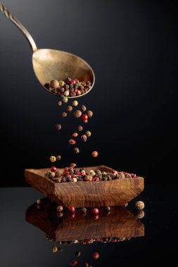 Siyah arka planda karabiber karışımı. Siyah, kırmızı, beyaz ve baharatlı biberler ahşap tabağa dökülür..