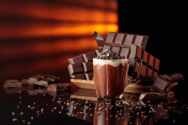 Çikolata kırıntıları serpiştirilmiş kremalı sıcak çikolata. Arka planda kırılmış acı çikolatalar. Siyah yansıtıcı arka plan. Boşluğu kopyala.