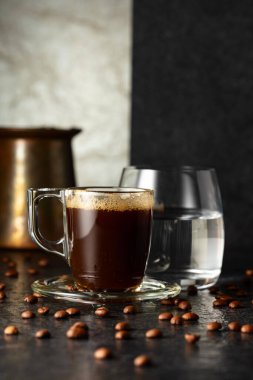 Espresso, bir bardak soğuk su ve arka planda kavrulmuş kahve çekirdekleri. Boşluğu kopyala.