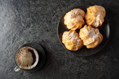 Kremalı kek ve sade kahve siyah taş bir masada. Üst görünüm.