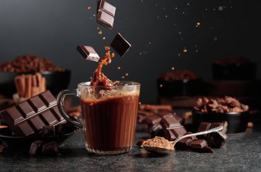Siyah mutfak masasının üzerinde malzemeler olan bir bardak sıcak çikolata. Kakao parçacıkları bir bardak kakao içeceğinin içine düşer ve güzel bir su sıçratır..