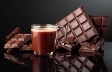 Bir bardak sıcak çikolata ve kırık acı çikolata. Kopyalama alanı olan siyah yansıtıcı arkaplan.