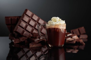 Krem şantili sıcak çikolata. Arka planda kırık bir çikolata parçasında. Kopyalama alanı olan siyah yansıtıcı arkaplan.