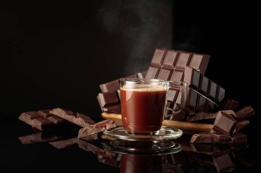Bir kupa sıcak çikolataya karşı kırık çikolatalar. Siyah parlak arka plan derinlik ve yansıma ekler. Boşluğu kopyala.