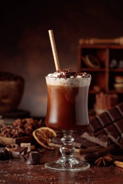 Üzerine krem şanti ve çikolata parçacıkları serpiştirilmiş sıcak çikolata. Eskimiş kahverengi arka planda yer alan malzemeler içeren bir çikolata içeceği..