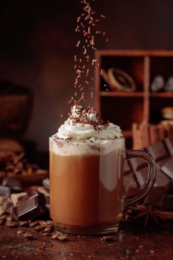 Üzerine krem şanti ve çikolata parçacıkları serpiştirilmiş çikolata içeceği. Eskimiş kahverengi arka planda yer alan malzemeler içeren bir çikolata içeceği..