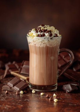 Krem şantili sıcak çikolata içeceği. Cam bardakta kakao ve koyu kahverengi arka planda acı çikolata..