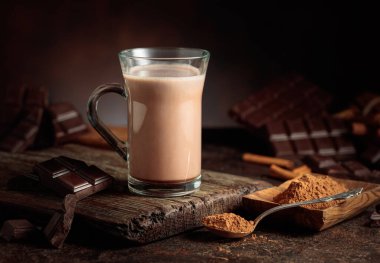 Kahverengi arka planda kremalı sıcak çikolata içeceği. Bir kupa sıcak çikolata, kırık çikolata ve kakao tozu. Boşluğu kopyala.