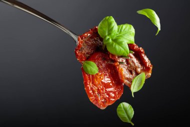 Yeşil fesleğenli zeytinyağında kurutulmuş domates. Siyah arka planda geleneksel İtalyan atıştırmalığı. Boşluğu kopyala. 