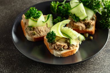 Pate, taze salatalık, kapari ve maydanozlu sandviç. Siyah tabakta ezmeli tost..
