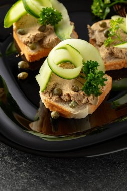 Pate, taze salatalık, kapari ve maydanozlu sandviç. Siyah tabakta ezmeli tost..