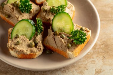Bej tabakta ezmeli tost. Pate, taze salatalık, kapari ve maydanozlu sandviç..