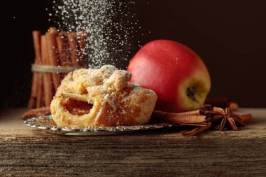 Eski ahşap masada elma ve tarçınlı Viyana turtası. Üzerine pudra şekeri serpilmiş taze pişmiş yiyecekler..