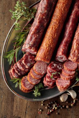 Biber, kekik, biberiye ve eski ahşap bir masada sarımsak ile dilimlenmiş kurutulmuş sosis. Üst görünüm.