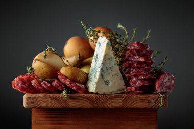 Mavi peynir, kurutulmuş sosisler, ahşap bir masada kekik ve armut..