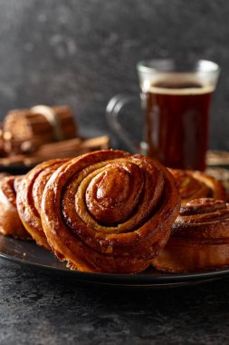 Kanelbullar - İsveç tarçınlı çörekler ya da dürümler. Siyah taş bir masada taze pişmiş çörekler..