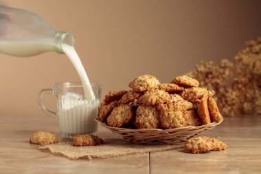 Yulaf ezmeli kurabiye ve süt mutfak masasında. Süt şişeden cam bardağa dökülür. Kopyalama alanı olan bej arkaplan.