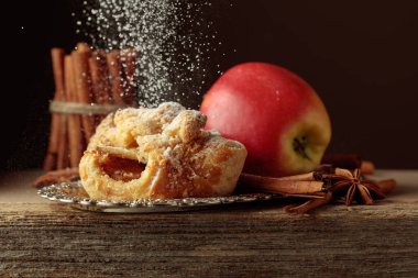 Eski ahşap masada elma ve tarçınlı Viyana turtası. Üzerine pudra şekeri serpilmiş taze pişmiş yiyecekler..