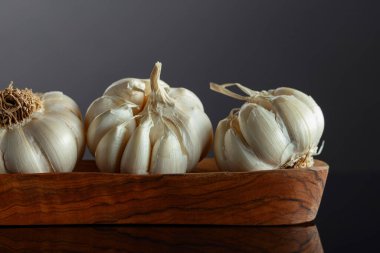 Siyah yansıtıcı arka planda ahşap kaptaki sarımsak soğanları. Boşluğu kopyala.
