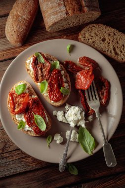 Ciabatta, zeytinyağı, ricotta ve fesleğende kurutulmuş domates. Eski ahşap bir masada geleneksel İtalyan atıştırması. Üst görünüm.