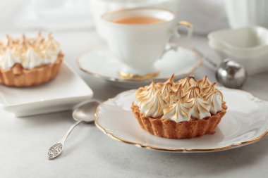 Beyaz bir masada kremalı turta. Kremalı turta, bir fincan çay ve beyaz mermer tezgahta beyaz mutfak aletleri..