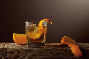 Kısa bardakta zengin bir Old Fashioned kokteyli, buzlu koyu kehribar likörü, eski ahşap bir tahtanın üzerinde portakal kabuğu ile süslenmiş. Boşluğu kopyala.