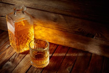 Zarif viski bardağı ve kehribar sıvısıyla dolu sürahi eski bir ahşap masada. Boşluğu kopyala.