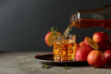 Apple kombucha şişeden bardağa dökülür. Eski bir mutfak masasında elmalı taze içecek. Boşluğu kopyala.