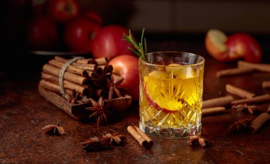 Elma dilimli elma şarabı ve biberiye filizi. Taze elmalar, tarçın çubukları ve anason eski bir mutfak masasına saçılmış..