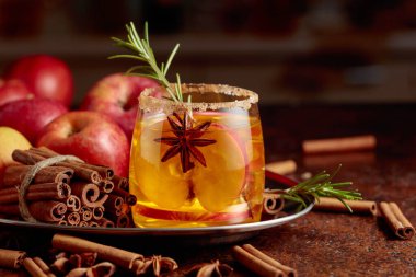 Elma dilimleri, anason ve biberiye dalıyla elmalı kombu çayı. Bardak şeker ve tarçın tozuyla süslenmiş..