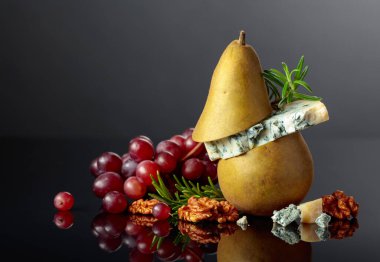 Armutlu mavi peynir, ceviz, kırmızı üzüm ve siyah arka planda biberiye. Siyah yansıtıcı arka planda meyveleri olan geleneksel küflü peynir. Boşluğu kopyala.