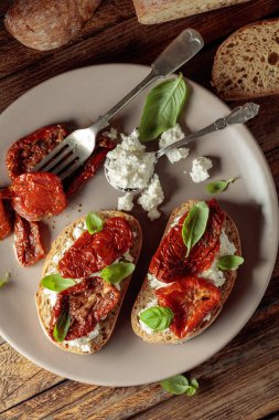 Ciabatta, zeytinyağı, ricotta ve fesleğende kurutulmuş domates. Eski ahşap bir masada geleneksel İtalyan atıştırması. Üst görünüm.