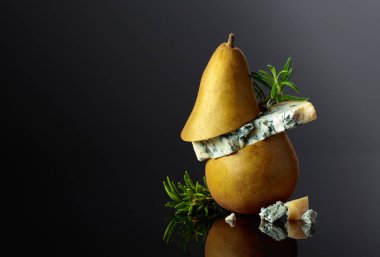 Siyah yansıtıcı arka planda armut ve biberiyeli mavi peynir. Boşluğu kopyala.