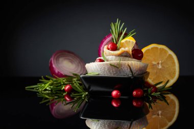 Limonlu balık fileto, kırmızı soğan ve kızılcıkla süslenmiş biberiye. Siyah yansıtıcı arka planda ringa balığı olan siyah bir tabak..