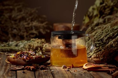 Sıcak su camdan bir çaydanlığa dökülüyor. Çeşitli kurutulmuş otlar ve baharatlar eski bir ahşap masaya serilmiştir. Aromaterapi ya da bitkisel tıp konsepti.