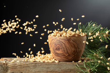 Siyah arka planda soyulmuş çam fıstığı. Tahta bir kasede fındıklar ve eski ahşap bir masada sedir dalı. Boşluğu kopyala.