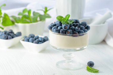 Mascarpone kreması, beyaz ahşap bir masada temiz bir kasede taze yaban mersini. Nane şekeriyle süslenmiş çilekli parfüm..