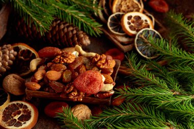 Kahverengi bir arka planda kurumuş meyve ve fındık. Kurutulmuş turunçgiller, kayısılar, kuru üzümler, çeşitli fındıklar, tarçın çubukları ve anason içeren bir Noel..