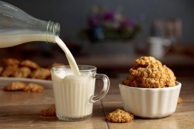 Mutfak masasında yulaflı kurabiye ve süt. Süt şişeden cam bardağa dökülür. Boşluğu kopyala.