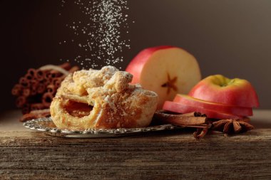 Eski ahşap masada elma ve tarçınlı Viyana turtası. Üzerine pudra şekeri serpilmiş taze pişmiş yiyecekler..