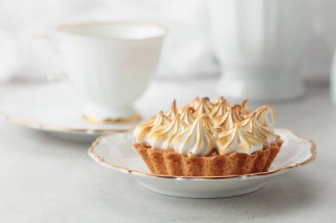 Beyaz bir masada kremalı turta. Kremalı turta, bir fincan çay ve beyaz mermer tezgahta beyaz mutfak aletleri..