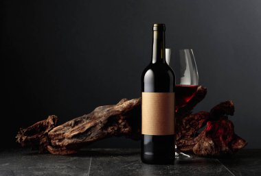 Boş etiketli bir şişe ve bir bardak kırmızı şarap. Arka planda eski yıpranmış bir pürüz var. Kopyalama alanı ile ön görünüm.