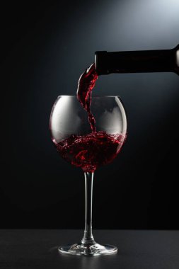 Kırmızı şarabı siyah arka planda bir şarap bardağına döküyorum..