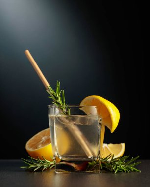 Buzlu, limonlu ve biberiyeli soğuk bir içecek. Siyah arka planda kokteyl cini ve tonik olan donmuş bardak..