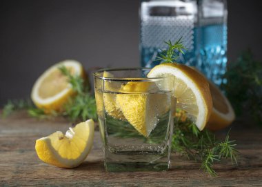 Eski ahşap bir masada cin, tonik ve limonlu kokteyl. Limon dilimleri ve ardıç dallı alkollü içecek..