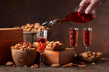 İtalyan likörü Amaretto. Eski bir masada badem fıstıklı. Likör şişeden bardağa dökülür..
