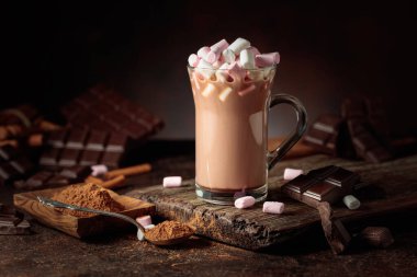 Kahverengi arka planda kremalı sıcak çikolata içeceği. Bir kupa sıcak çikolata, kırık çikolata ve kakao tozu. Boşluğu kopyala.