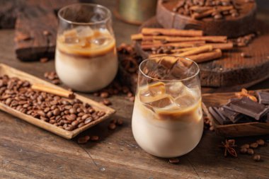 Eski ahşap arka planda buzlu bardakta İrlanda kreması ve kahve kokteyli. Kahve çekirdekleri, tarçın, anason ve çikolata parçaları masaya saçıldı.. 