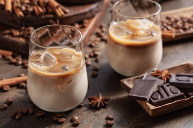 Eski ahşap arka planda buzlu bardakta İrlanda kreması ve kahve kokteyli. Kahve çekirdekleri, tarçın, anason ve çikolata parçaları masaya saçıldı.. 