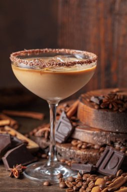 Eski ahşap arka planda buzlu bir bardakta İrlanda kreması ve kahve kokteyli. Kahve çekirdekleri, tarçın, anason ve çikolata parçaları masaya saçıldı.. 